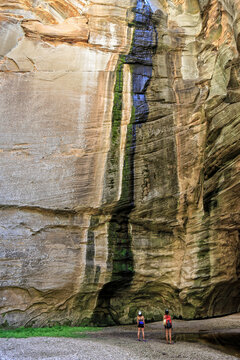 Two girls stand beneath a cliff of sandstone in Sundance Slot Canyon, Coconino National Forest, Arizona
