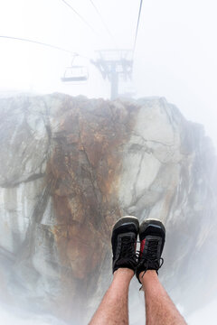 Man wearing running shoes riding Peak Chair chairlift on Whistler Backcomb, Whistler, British Columbia, Canada