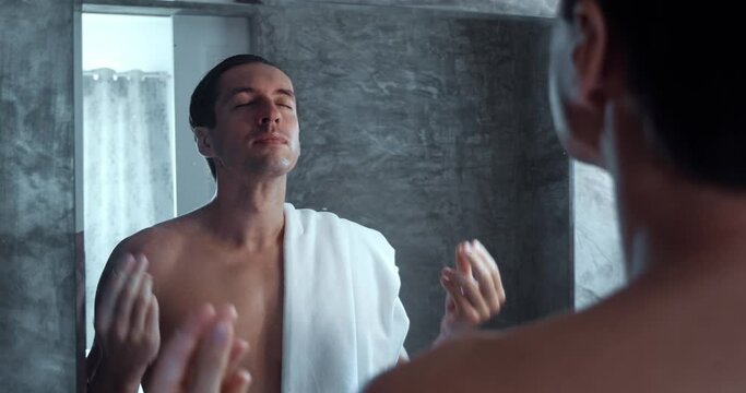 Man stands in the bathroom looks at himself in the mirror and puts himself in order, fixes himself. Young man motivates himself relieves stress and prepares for new day, standing in the bathroom