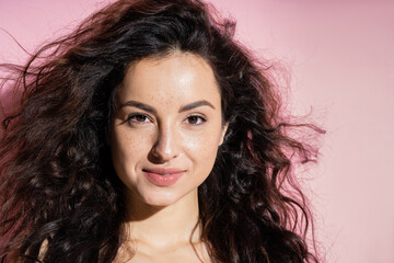 Freckled brunette woman smiling at camera on pink background.