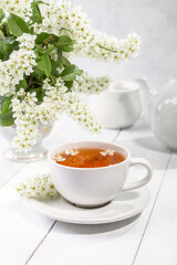Obraz na płótnie Canvas Useful spring tea with bird cherry in a white cup on a light background