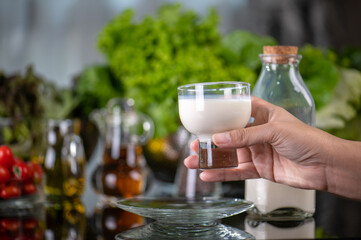 hand hold glass of milk after pours the milk into glass. Serving breakfast fresh milk in glass on glass kitchen table. Front view of healthy drink in breakfast	
