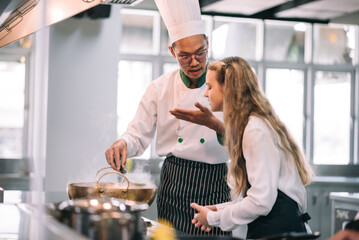 Mature asian teacher teaching schoolgirl chef students to cooking in class. Mature chef with kids at school.