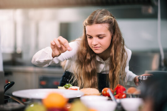 Caucasian schoolgirl concentrated to learning cooking in the kitchen with professional chef at school.