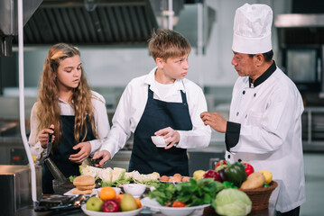 Group of diverse student chef learning cooking class in the kitchen. Mature asian teacher teaching diverse chef students at school.