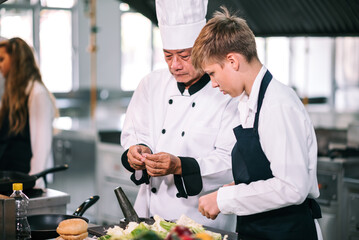 Group of diverse student chef learning cooking class in the kitchen. Mature asian teacher teaching diverse chef students at school.