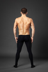 Portrait of a young ballet dancer photographed from behind, standing in front of a gray background.