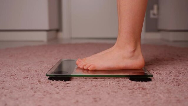 Girls legs on the scales close-up. Young female person measure body weight mass on transparent glass scales. Caucasian child is barefoot. Normal weight and healthy lifestyle concept