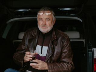 Portrait of gray-haired man with glass of whiskey in car