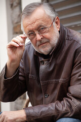 Handsome elderly man in glasses and leather jacket close-up