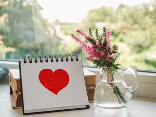 Notepad and painted heart on the background of the window. Daylight. Close-up, indoors. Congratulations for family, relatives, loved ones, friends and colleagues