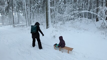 Mutter zieht Kind auf Schlitten durch den Schnee