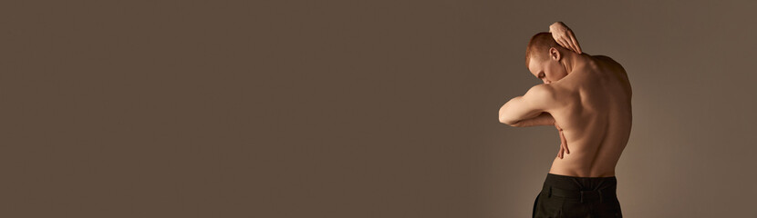 Fototapeta premium Relief, strong, muscular male back. Young man posing shirtless in pants over light brown studio background. Concept of men's health and beauty, body care, fitness. Banner. Copy space for ad, text