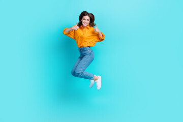 Fototapeta na wymiar Full length photo of excited confident lady wear orange shirt jumping high showing thumb up isolated turquoise color background
