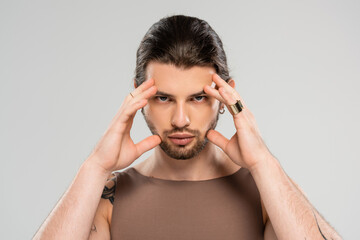 Portrait of brunette and tattooed man touching face isolated on grey.