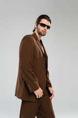 Trendy man in suit and sunglasses standing isolated on grey.