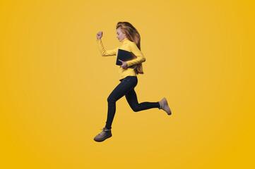 Fototapeta na wymiar Full body of a young happy woman jumping, running holding modern device isolated on yellow color background. People lifestyle fashion concept