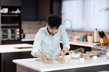 Fototapeta premium Hispanic young man baking homemade cookies - young man preparing cookies - pastry man