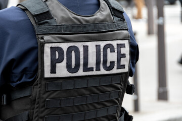 Marquage "POLICE" en gros plan écrit à l'arrière d'un gilet pare-balles porté par un officier de police dans une rue de Paris, France. Concepts de délinquance, d'enquêtes et d'affaires criminelles