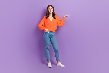 Full length size cadre of young positive promoter girl wearing orange jumper hold palm offer cheap proposition isolated on purple color background