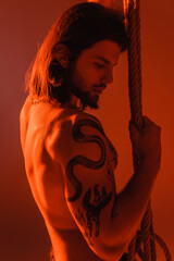 Sexy tattooed model holding rope isolated on red.