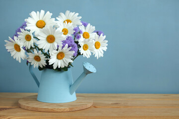 bouquet of daisies and ageratum in a watering can on a table.