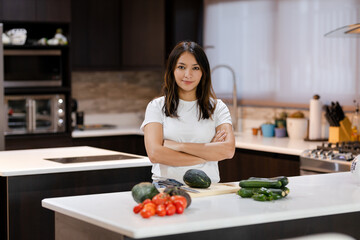 Obraz na płótnie Canvas Young hispanic woman proud of her healthy food - woman with vegetables in her kitchen ready to prepare vegan food