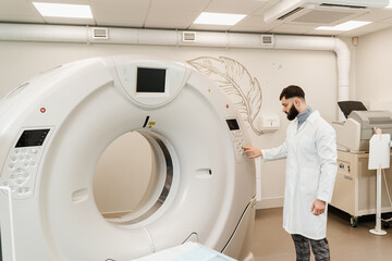 Man doctor adjusts CT computed tomography scanner in medical clinic. Handsome bearded radiologist...