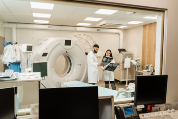 Colleague doctors discussing x-rays in the CT computed tomography scan room. Medical doctor intern girl is studying in the CT computed tomography scanning room at internship courses.