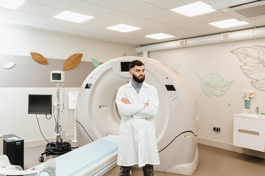Handsome bearded doctor in medical robe with computed tomograph for obtain detailed internal images of the body of patient. Man doctor in CT scan computed tomography room in medical clinic.