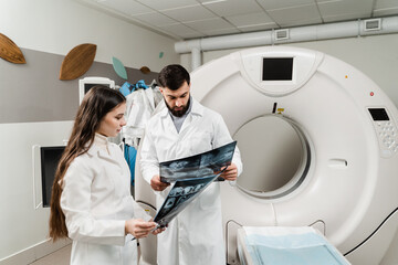 Colleague doctors discussing x-rays in the CT computed tomography scan room. Medical doctor intern girl is studying in the CT computed tomography scanning room at internship courses.