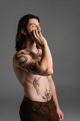 Long haired and tattooed model touching face isolated on grey.