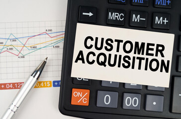 On the business chart lies a pen, a calculator and a business card with the inscription - Customer Acquisition