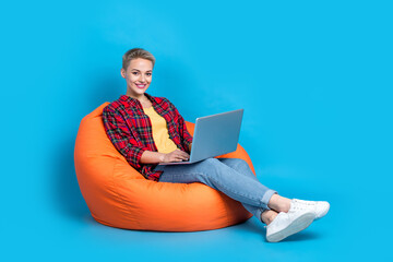 Full size photo of cheerful girl with short hairstyle wear red shirt sit in armchair chatting laptop isolated on blue color background