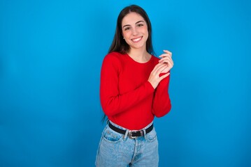 young brunette girl wearing red T-shirt against blue wall clapping and applauding happy and joyful,...