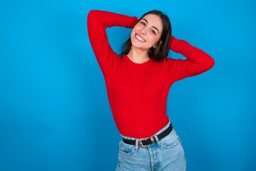 young brunette girl wearing red T-shirt against blue wall stretching arms, relaxed position.