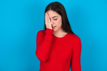 young brunette girl wearing red T-shirt against blue wall Yawning tired covering half face, eye and mouth with hand. Face hurts in pain.