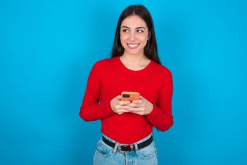 young brunette girl wearing red T-shirt against blue wall holding in hands showing new cell