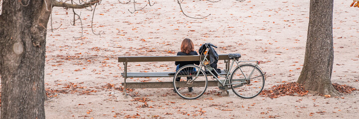 Lonely woman sitting on a bench with her bike on an Autumn day in the Tuileries garden in Paris,...