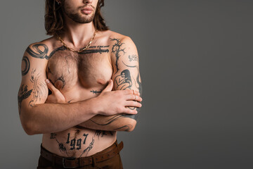 Cropped view of long haired and tattooed man crossing arms isolated on grey.