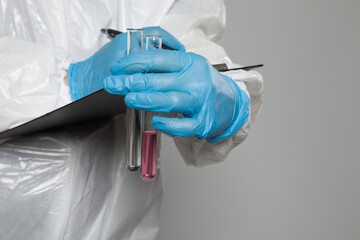 Laboratory worker holding test tubes with substance samples for analysis and taking notes on gray...