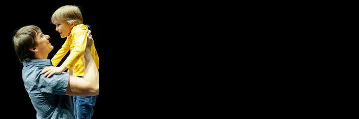 man father dad holds little kid boy son six years old in his arms and hugs. happy family, parenthood, fatherhood and childhood isolated on black background. banner. mockup and space for text