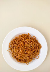 Plate with wholemeal spaghetti pasta and pieces of garlic on a white background