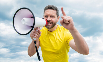 man in yellow shirt shout in loudspeaker on sky background. pointing finger