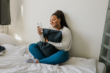 Happy modern African American young girl talking on video chat and sit at home communication concept. Smiling hipster girl making self portrait on her telephone at home