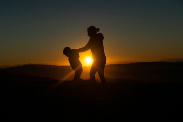 Fototapeta na wymiar Mother and son silhouetted at sunset when walking