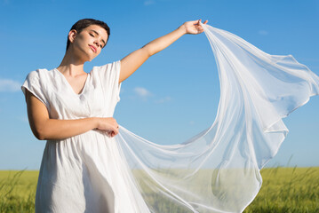 Portrait of a beautiful young smiling woman in summer nature playing with a white veil	