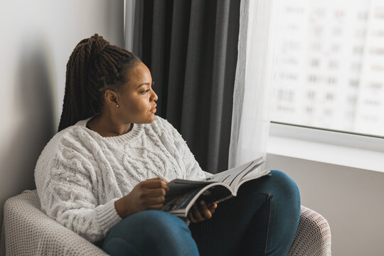 african american woman with dreadlocks reading magazine at home - leisure and lifestyle concept