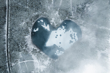 Aerial image of a heart shaped frozen lake surrounded by snow covered forest,
