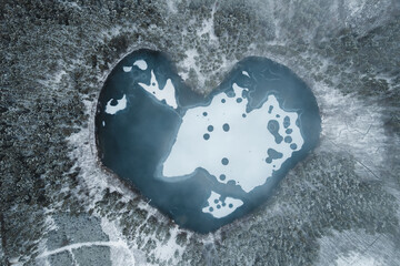 Aerial image of a heart shaped frozen lake surrounded by snow covered forest,